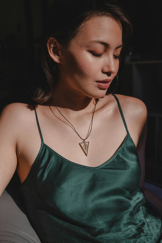 Woman in a deep green satin camisole wearing a geometric pendant necklace, captured in soft natural light